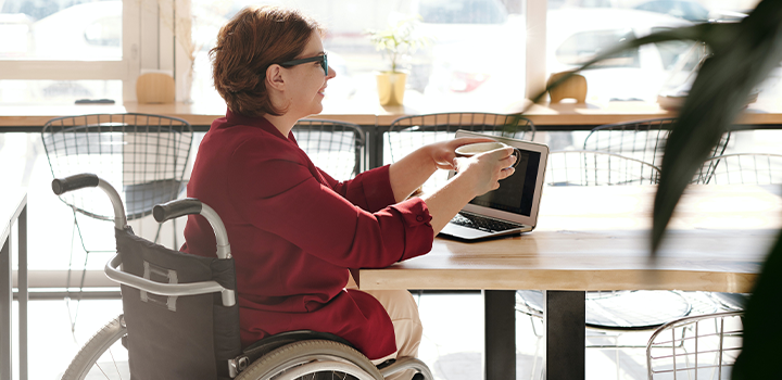 Mujer usuaria de silla de ruedas en un computador, en una cafetería